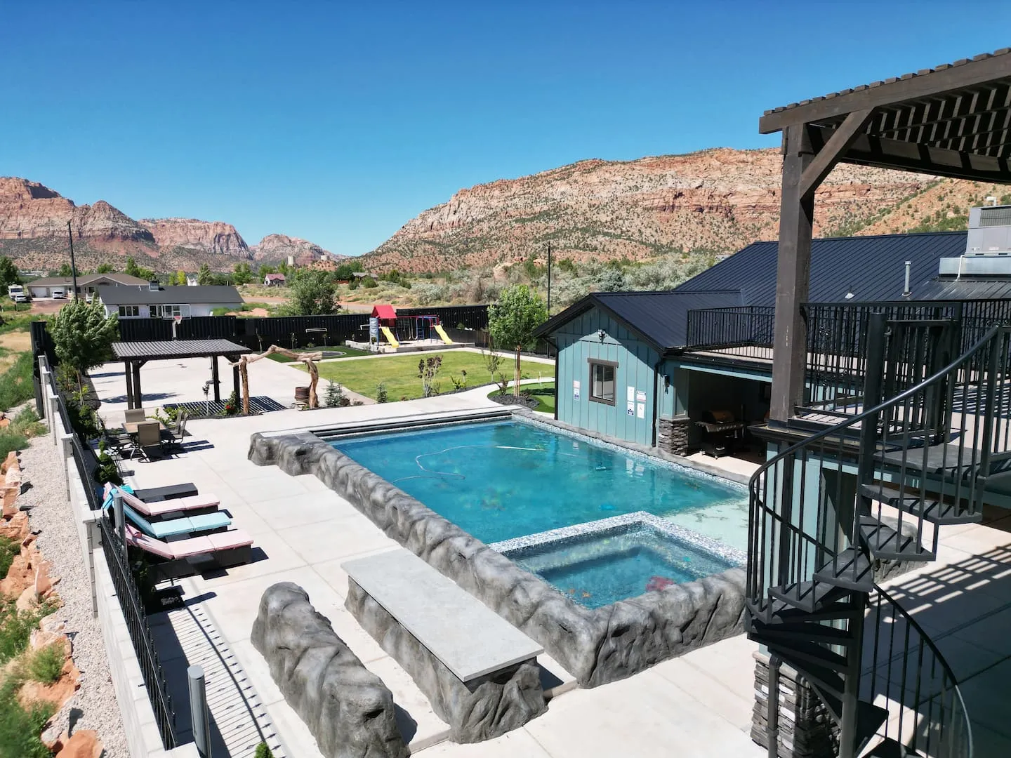 Heated pool and hot tub with lounge chairs, red rock cliffs behind the backyard