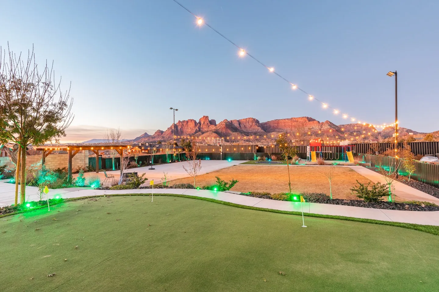 Backyard putting green under string lights at dusk with mountains beyond